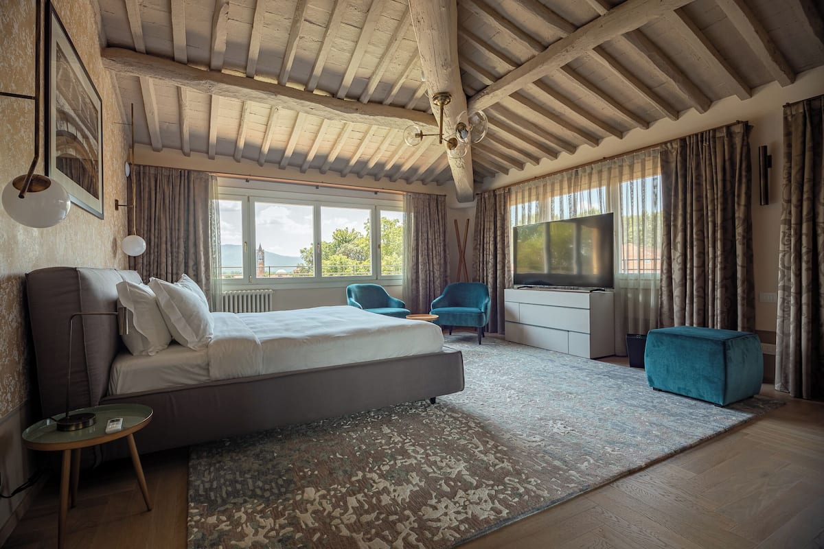 Ein Schlafzimmer mit einem großen Bett, einem Schreibtisch, einem Fernseher und Blick ins Freie.