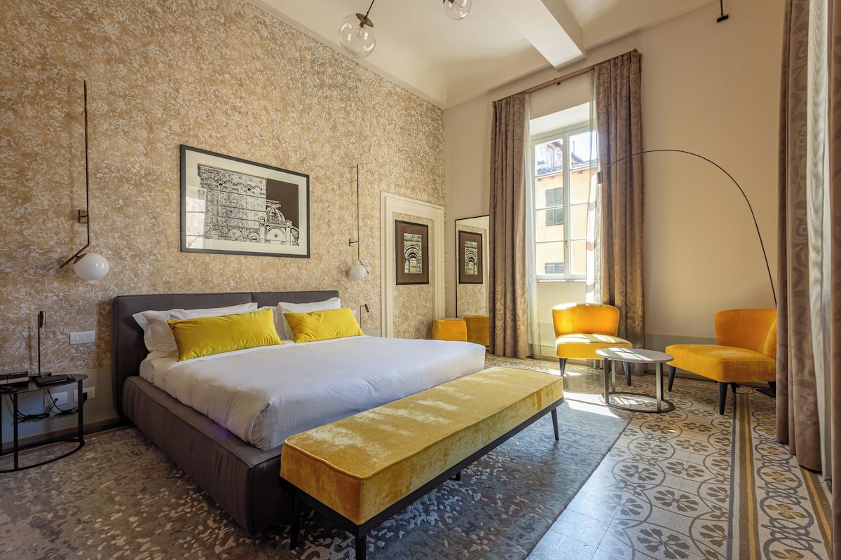 Ein Hotelzimmer mit einem großen Bett, einer Bank, einem Schreibtisch und einem Sessel.