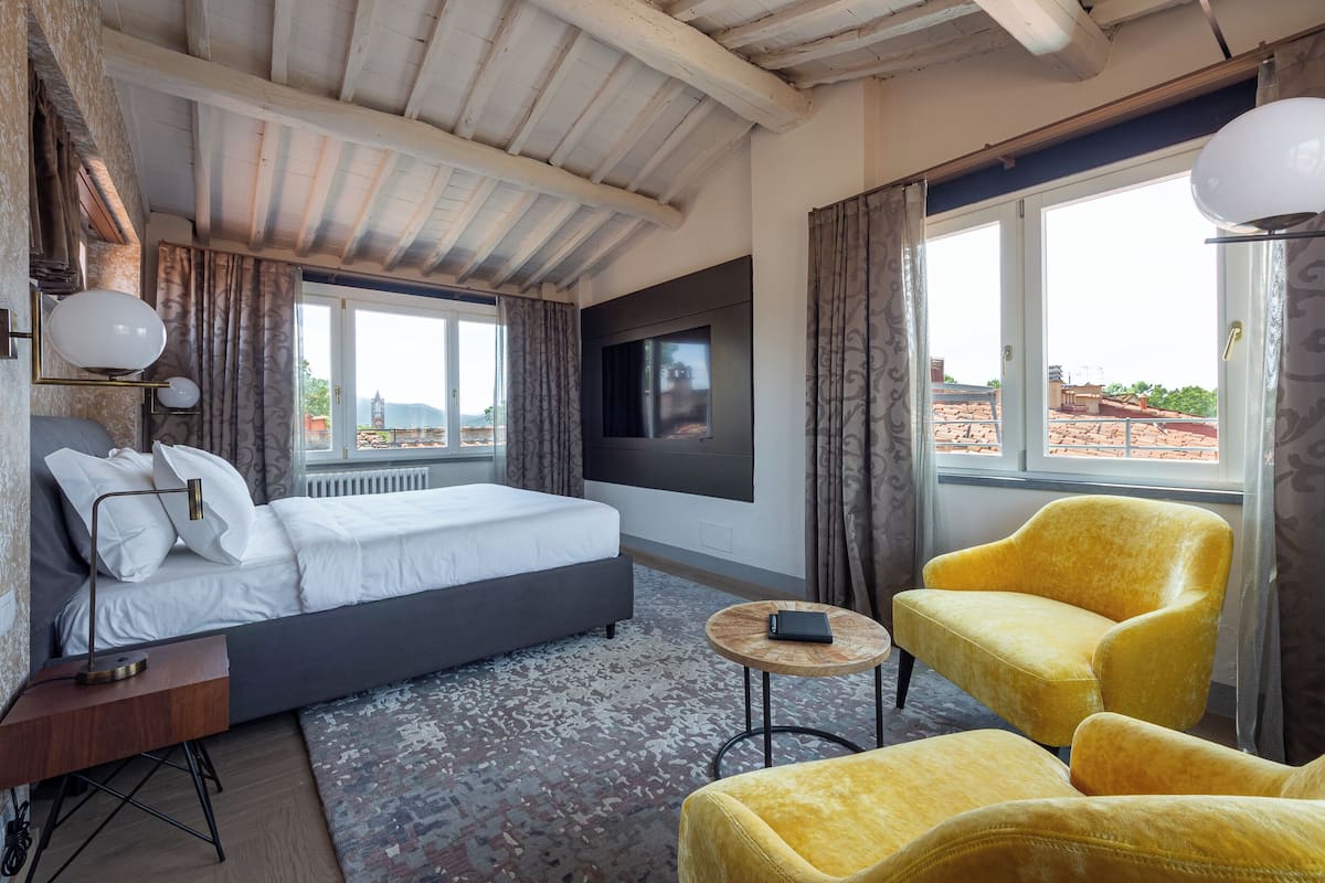 Ein Schlafzimmer mit einem Bett, einem Fernseher, einem kleinen runden Tisch und zwei gelben Sesseln.