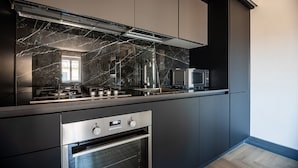 A modern kitchen with dark cabinetry, a marble backsplash, stainless steel appliances, and a built-in oven.