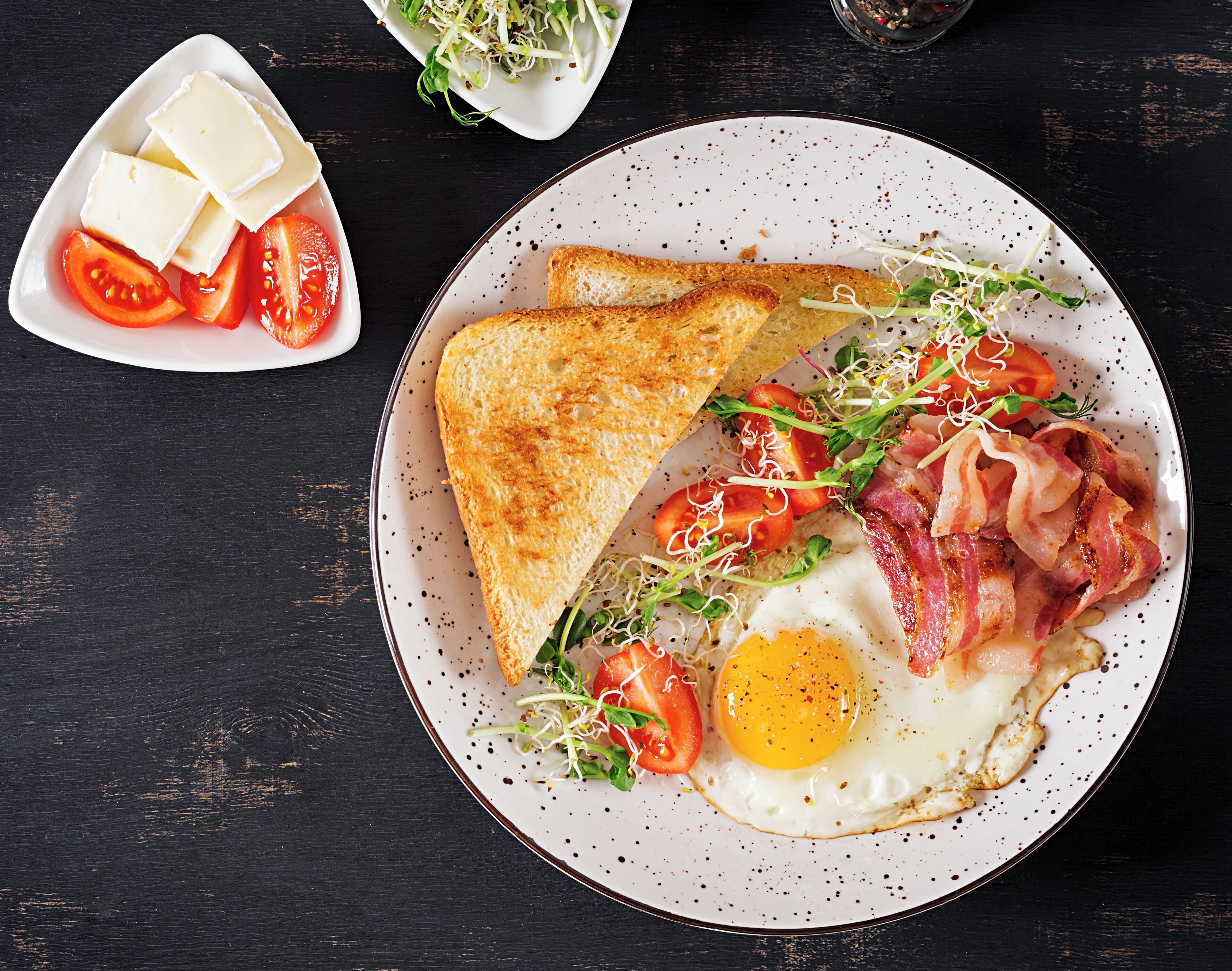 Um prato com torradas, bacon, ovo e rodelas de tomate.