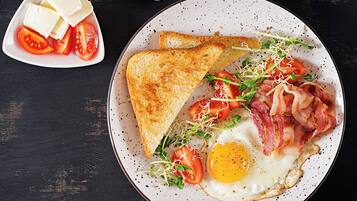 Um prato com torradas, bacon, ovo e rodelas de tomate.