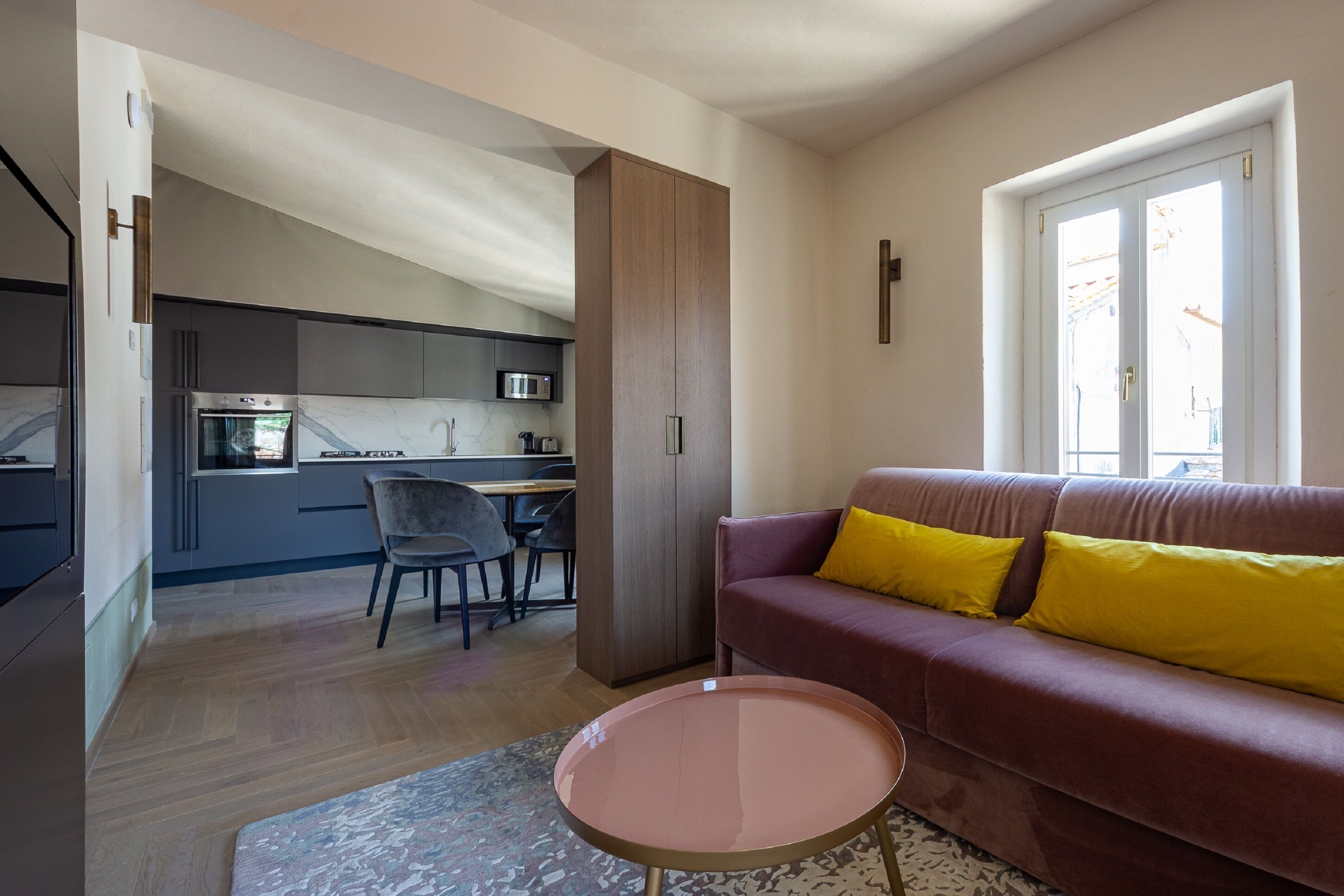A modern living room with a sofa, a coffee table, and a dining area with chairs and a kitchen in the background.