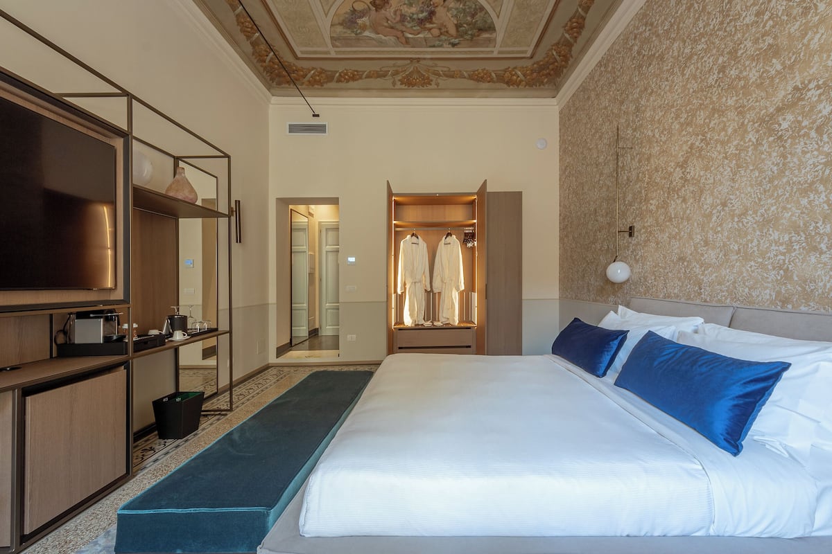 Ein Hotelzimmer mit einem großen Bett, einem Kleiderschrank, einem Schreibtisch mit Flachbildfernseher und einem Spiegel.