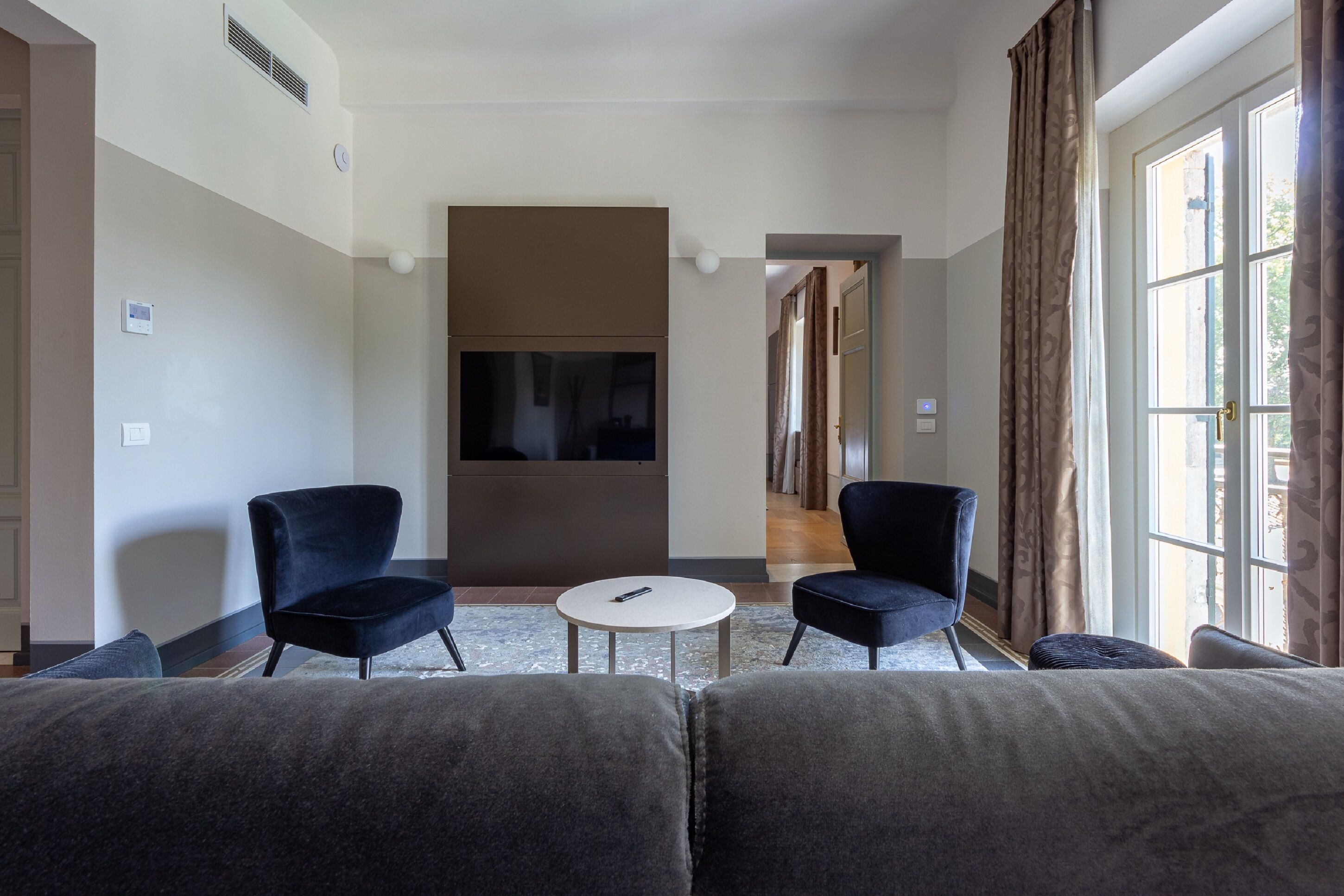 A modern hotel room with a large bed, two armchairs, a small round table, and a TV.
