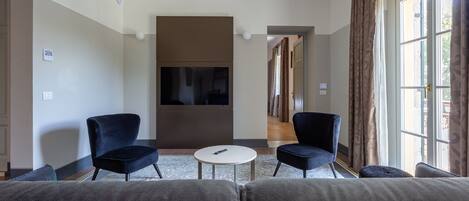 A modern hotel room with a large bed, two armchairs, a small round table, and a TV.