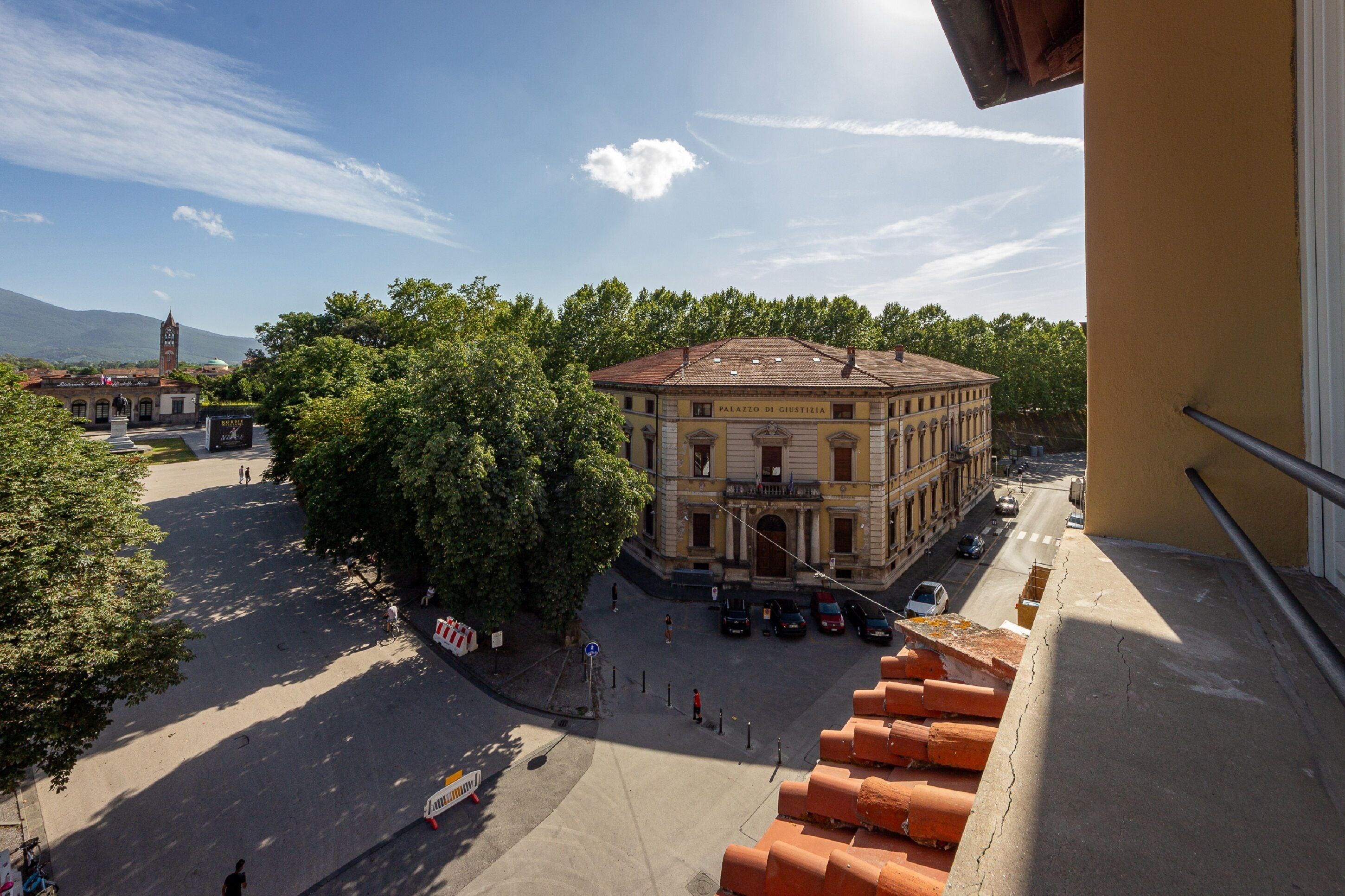Blick auf ein historisches Gebäude mit einem zentralen Innenhof, umgeben von Bäumen und blauem Himmel.