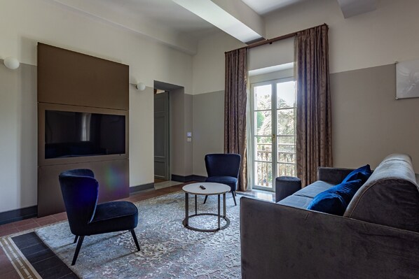 A modern living room with a flat-screen TV, a sofa, a chair, and a small round table. - Grand Universe La Residenza (Lucca)