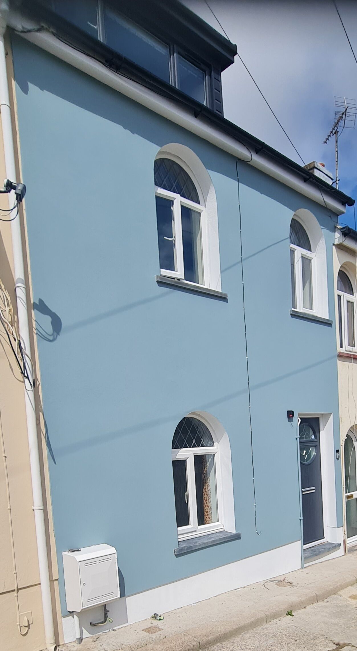 A two-story building with a light blue exterior, white window frames, and a black door.