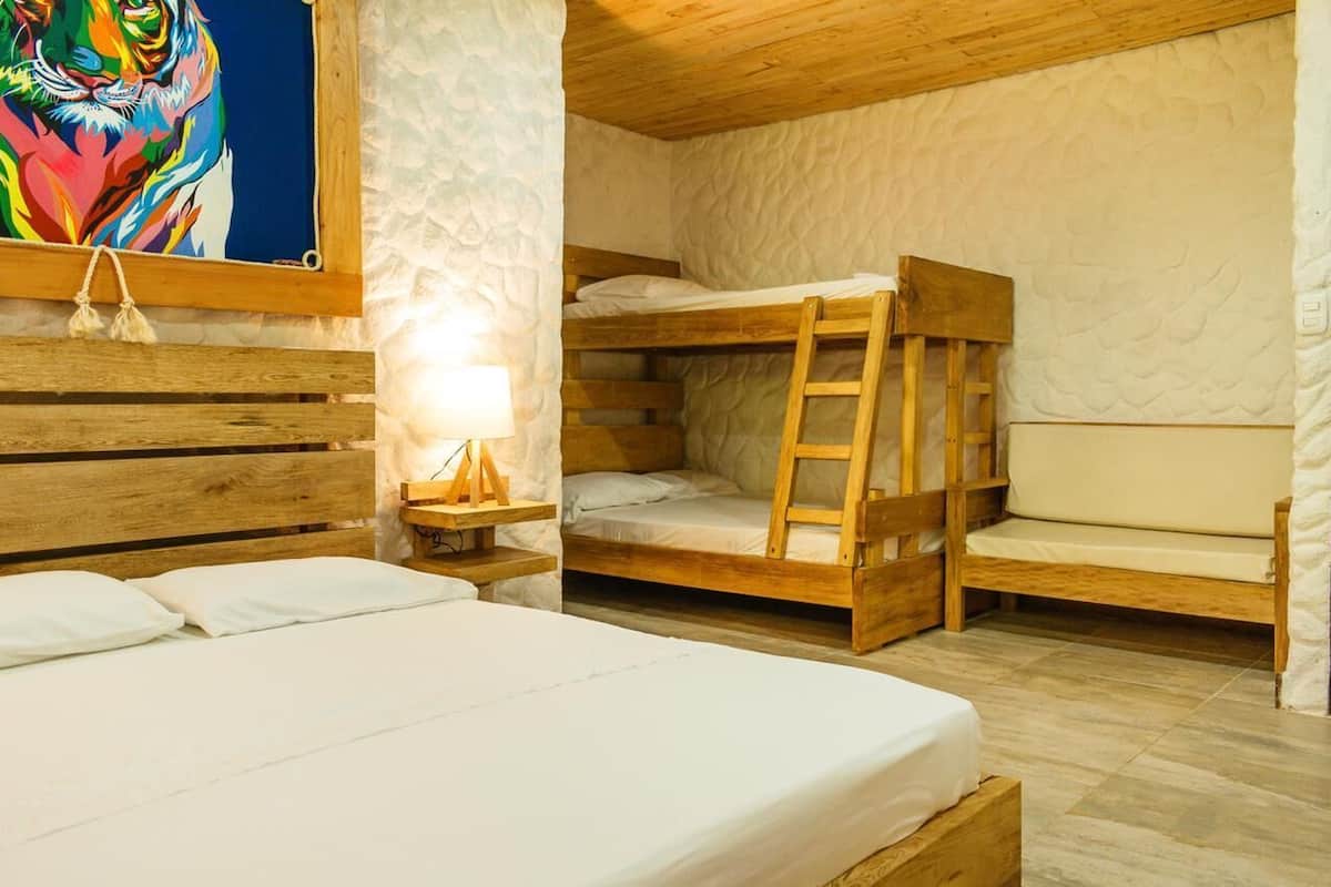A room with bunk beds, a wooden headboard, a bedside table with a lamp, and a colorful painting on the wall.