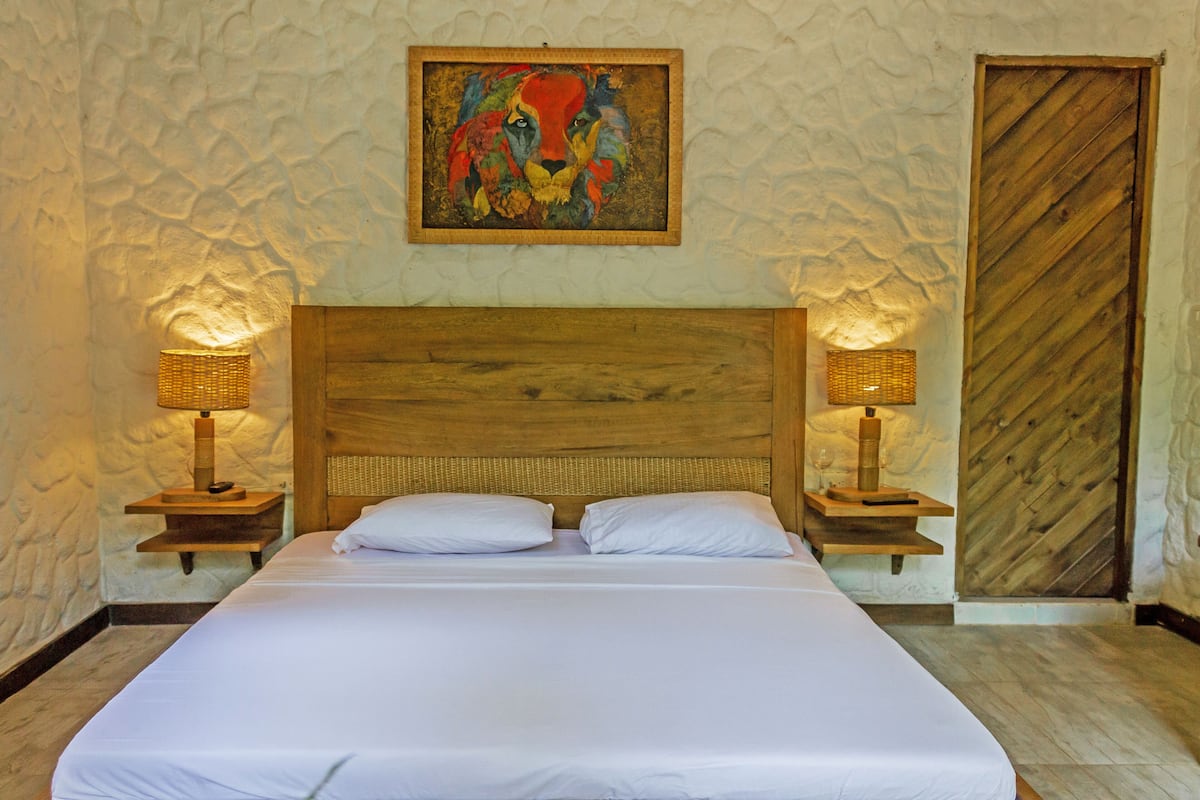 A large bed with white linens, two bedside lamps, a wooden headboard, and a textured wall.
