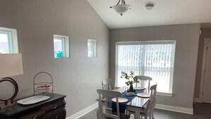 A dining area with a table set for four, surrounded by white chairs, a dark wooden dresser, and a window with blinds. - Bettendorf Condo: 2BR, 2BA, Garage, King master, Pets Welcome! (Bettendorf)