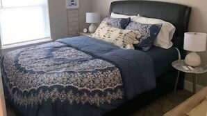 A bedroom with a large bed, two bedside tables, a nightstand, a window, and a door. - Bettendorf Condo: 2BR, 2BA, Garage, King master, Pets Welcome! (Bettendorf)