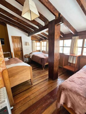 Een eenvoudige kamer met houten vloeren, twee bedden met roze beddengoed, een houten stoel, een tafel en een hanglamp.