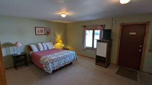 A bedroom with a bed, bedside lamps, a TV on a stand, a door, and a window with curtains. - Nova Motel (Ludington)