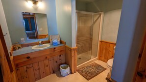 A bathroom with wooden cabinetry, a double sink, a large mirror, a shower with glass doors, and a toilet. - Nova Motel (Ludington)
