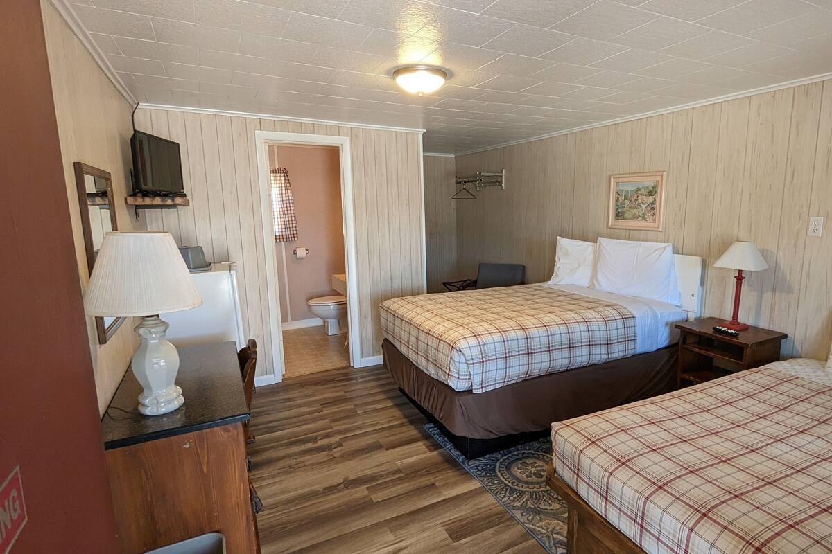 A bedroom with two beds, a desk, a chair, a TV, and a bathroom.