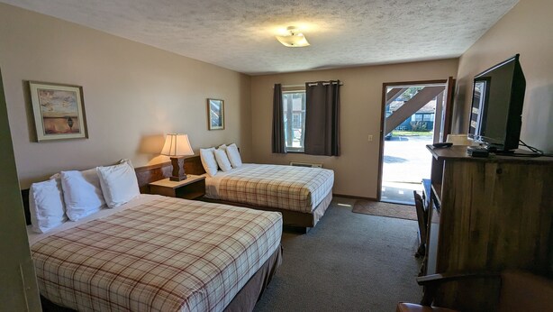 A hotel room with two beds, a desk, a lamp, a television, and a view of the outside. - Nova Motel (Ludington)