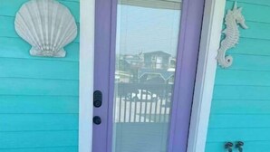 A turquoise house with a purple door, a white seahorse decoration, and a welcome mat reading "Welcome to CASTAWAVES".