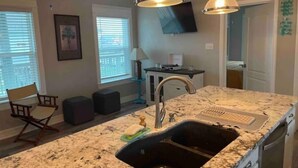 A kitchen with a granite countertop, double sink, and pendant lighting.