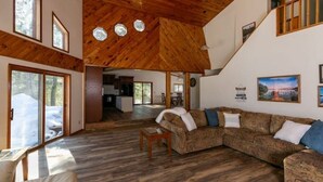 A spacious living area with a wooden ceiling, large windows, and a built-in fireplace. - Waterfront Peninsula Escape Cabin (Lakewood)