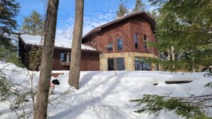 A large, multi-story wooden house with a sloped roof, surrounded by snow-covered ground and trees. - Waterfront Peninsula Escape Cabin (Lakewood)