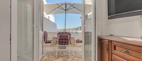 A room with a sliding glass door leading to an outdoor patio area with a table and chairs, a large umbrella, and a television mounted on the wall.