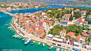 A coastal town with a marina, buildings with red roofs, and a clear blue sea.