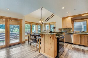A spacious kitchen with wooden cabinets, a central island, and large windows offering views of the outdoors. - Deer Valley Condo Retreat Close to Skiing Hiking Hot Tub 402 (Park City)