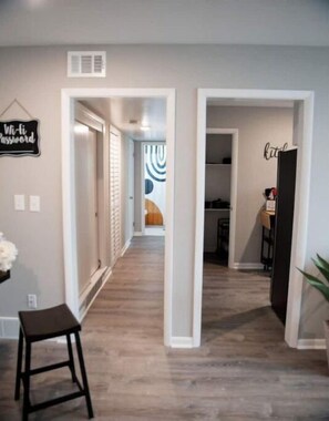 Stylish hallway with a large window leading to a room, featuring a black-framed picture frame and a stool.
