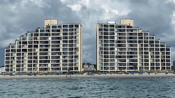 Un hotel sulla spiaggia con diversi piani, balconi e vista mare.