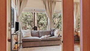 A cozy living room with a sofa, a ceiling fan, and a view of trees outside.