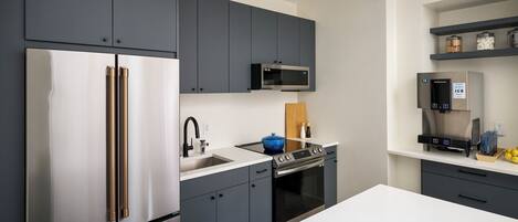 A modern kitchen with stainless steel appliances, grey cabinetry, and a white countertop.