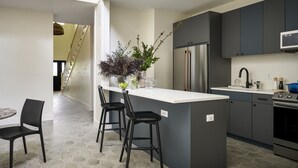 A modern kitchen with a central island, bar stools, a refrigerator, and a microwave. - The Neighborhood Hotel-New Buffalo (New Buffalo)
