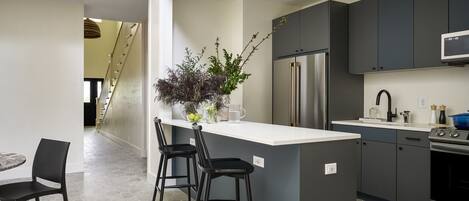 A modern kitchen with a central island, bar stools, a refrigerator, and a microwave.