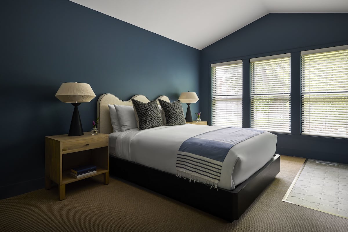 A bedroom with a bed, two bedside tables, and a window with blinds.
