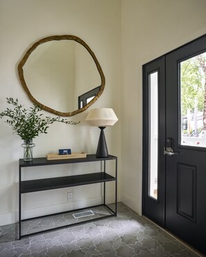 A black door with a window, a black console table with a lamp, a mirror, and a plant. - The Neighborhood Hotel-New Buffalo (New Buffalo)
