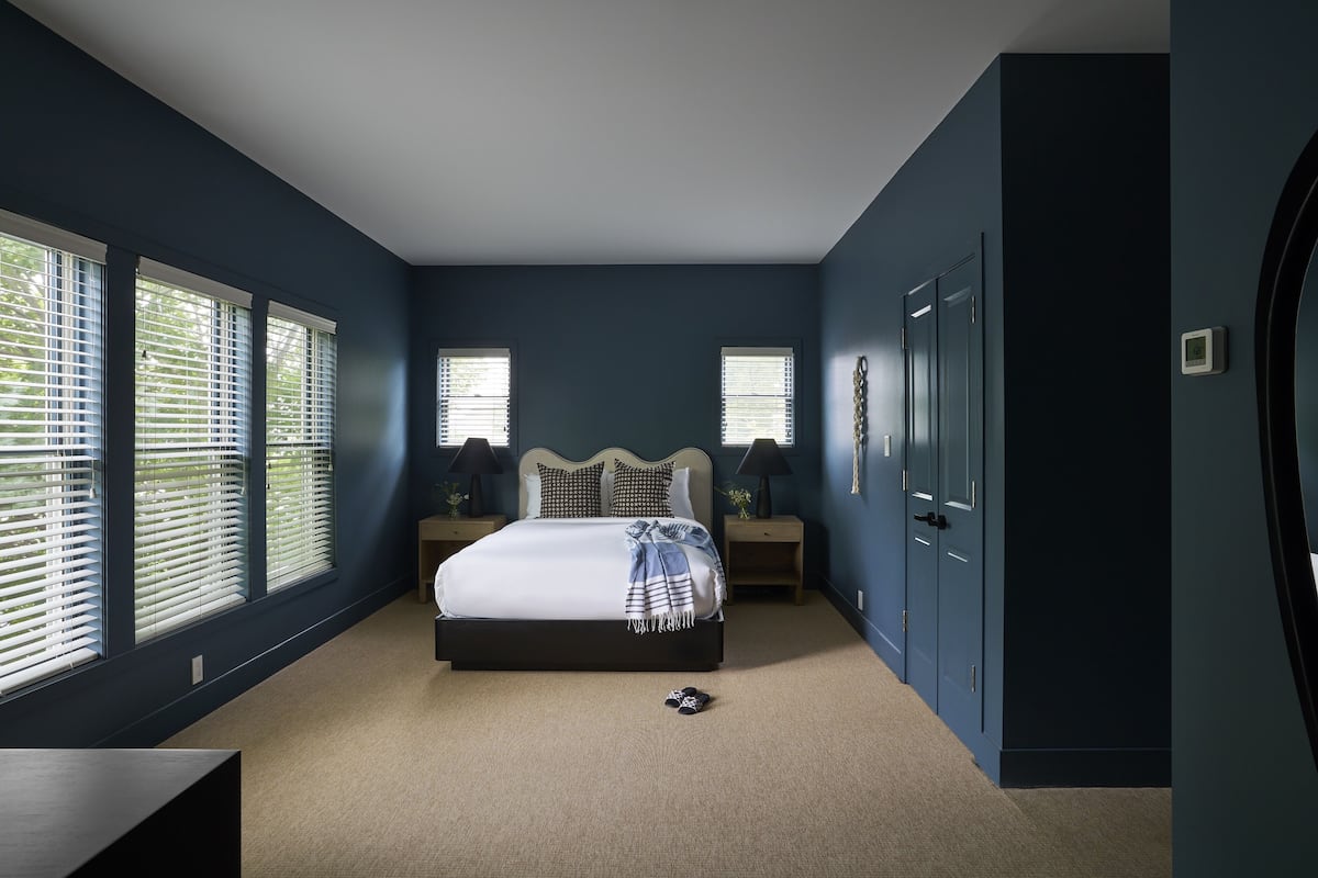 A bedroom with a large bed, two bedside tables, a wardrobe, and a window with blinds.