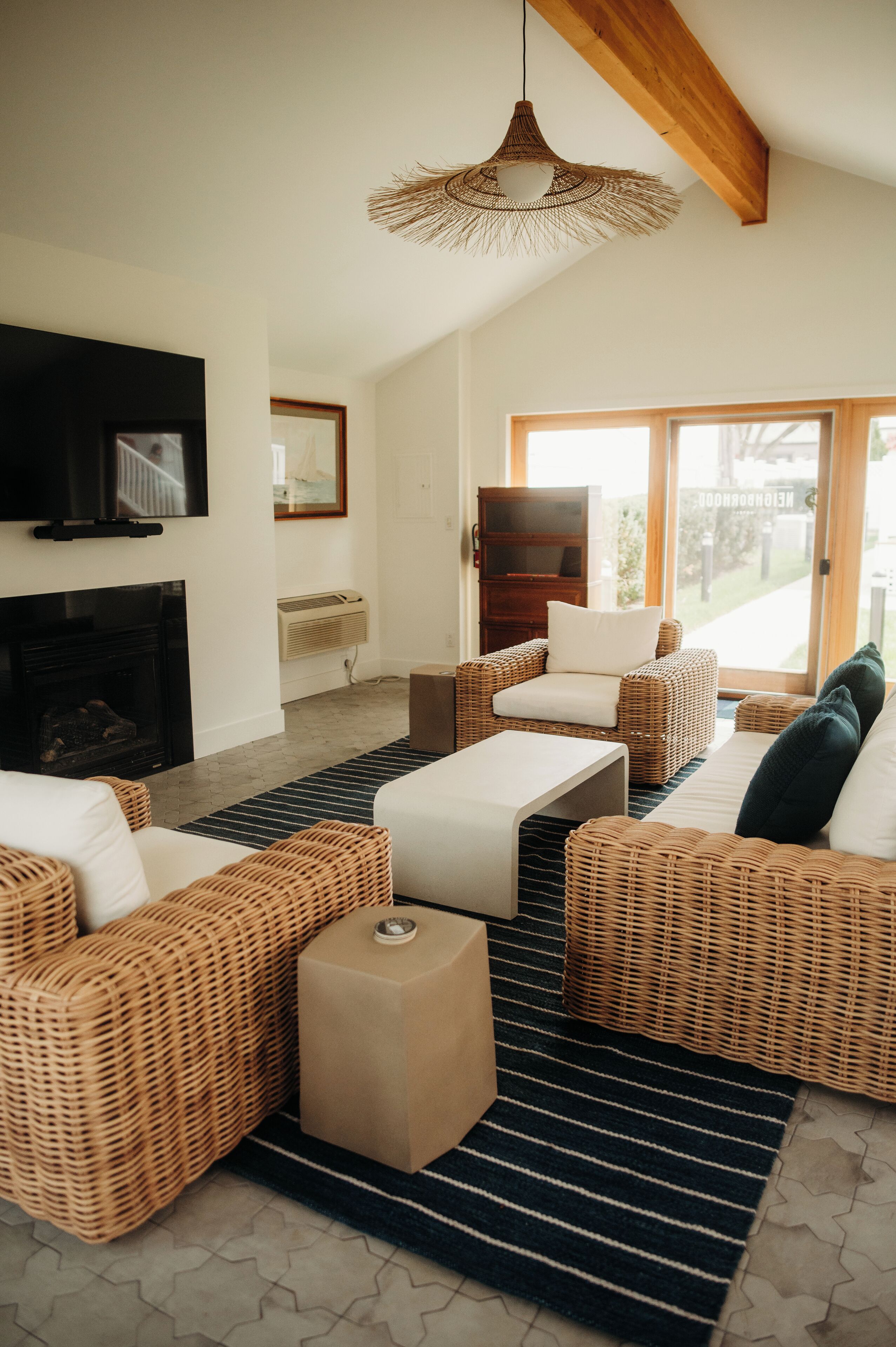 A living room with wicker furniture, a flat-screen TV, a fireplace, and a large window with a view.