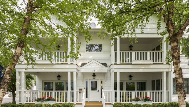 A two-story white building with a front porch, a central door, and a number '18' above the door. - The Neighborhood Hotel-New Buffalo (New Buffalo)