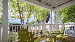 A covered porch with two green Adirondack chairs, a small table, and a flag. - The Neighborhood Hotel-New Buffalo (New Buffalo)