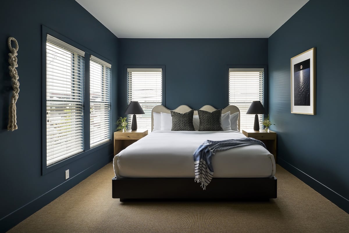 A bedroom with a large bed, two bedside tables, a wall-mounted lamp, and a framed picture.