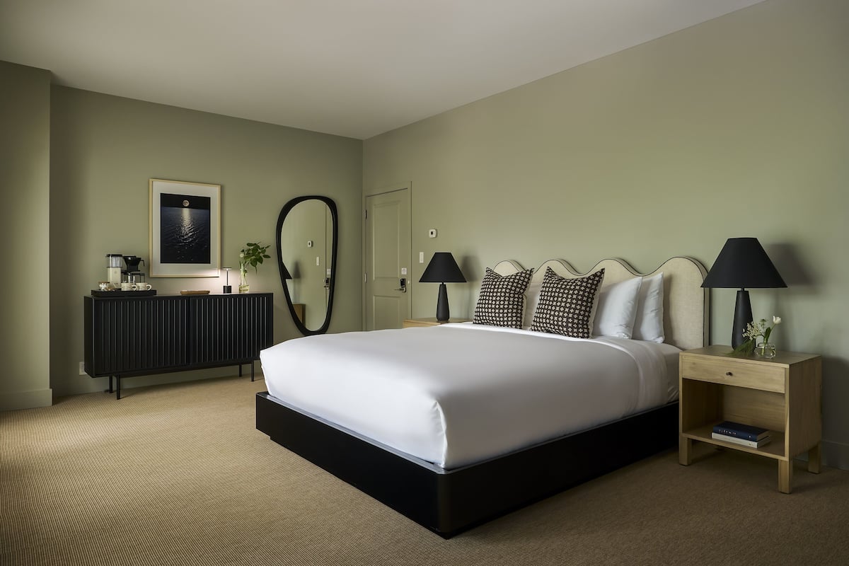 A neatly arranged bedroom with a large bed, bedside tables, a dresser, and a mirror.