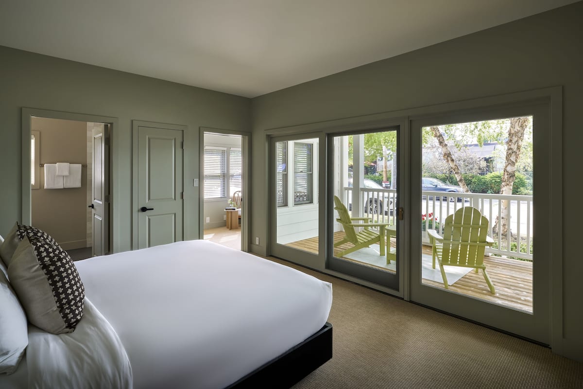 A bedroom with a large bed, a door leading to a bathroom, and a sliding glass door to an outdoor deck with a chair.