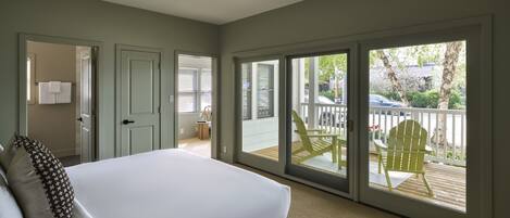 Une chambre avec un grand lit, une porte donnant sur une salle de bain et une porte-fenêtre coulissante qui mène à une terrasse extérieure avec un fauteuil.