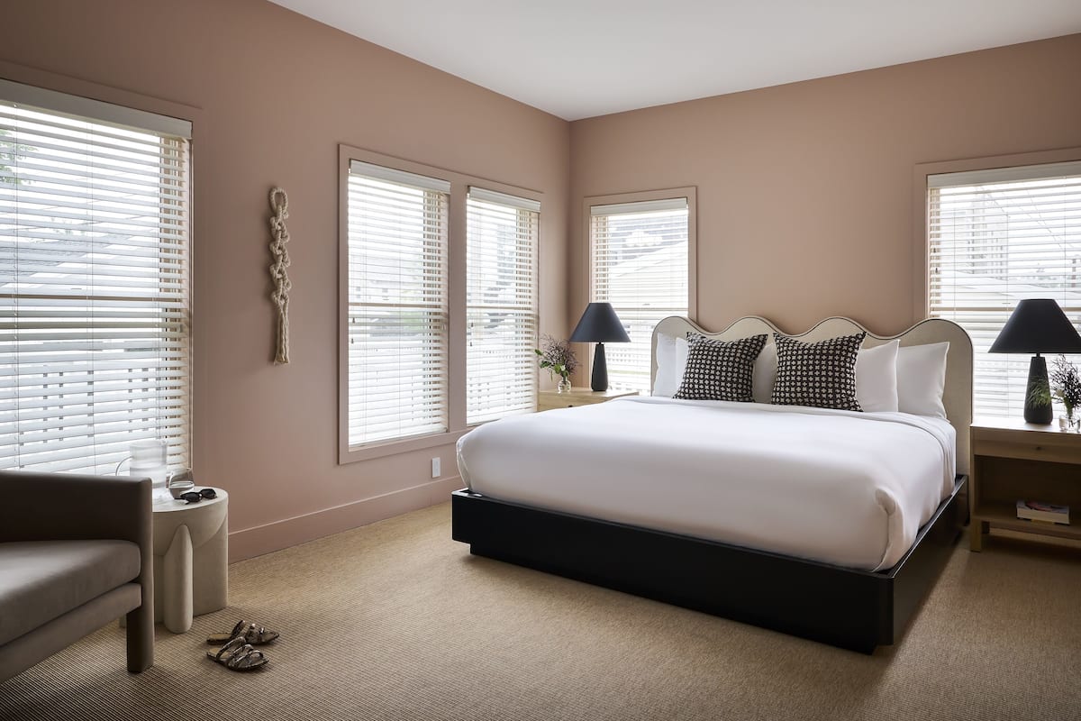 A bedroom with a large bed, two bedside tables with lamps, a chair, and a small table with a plant.