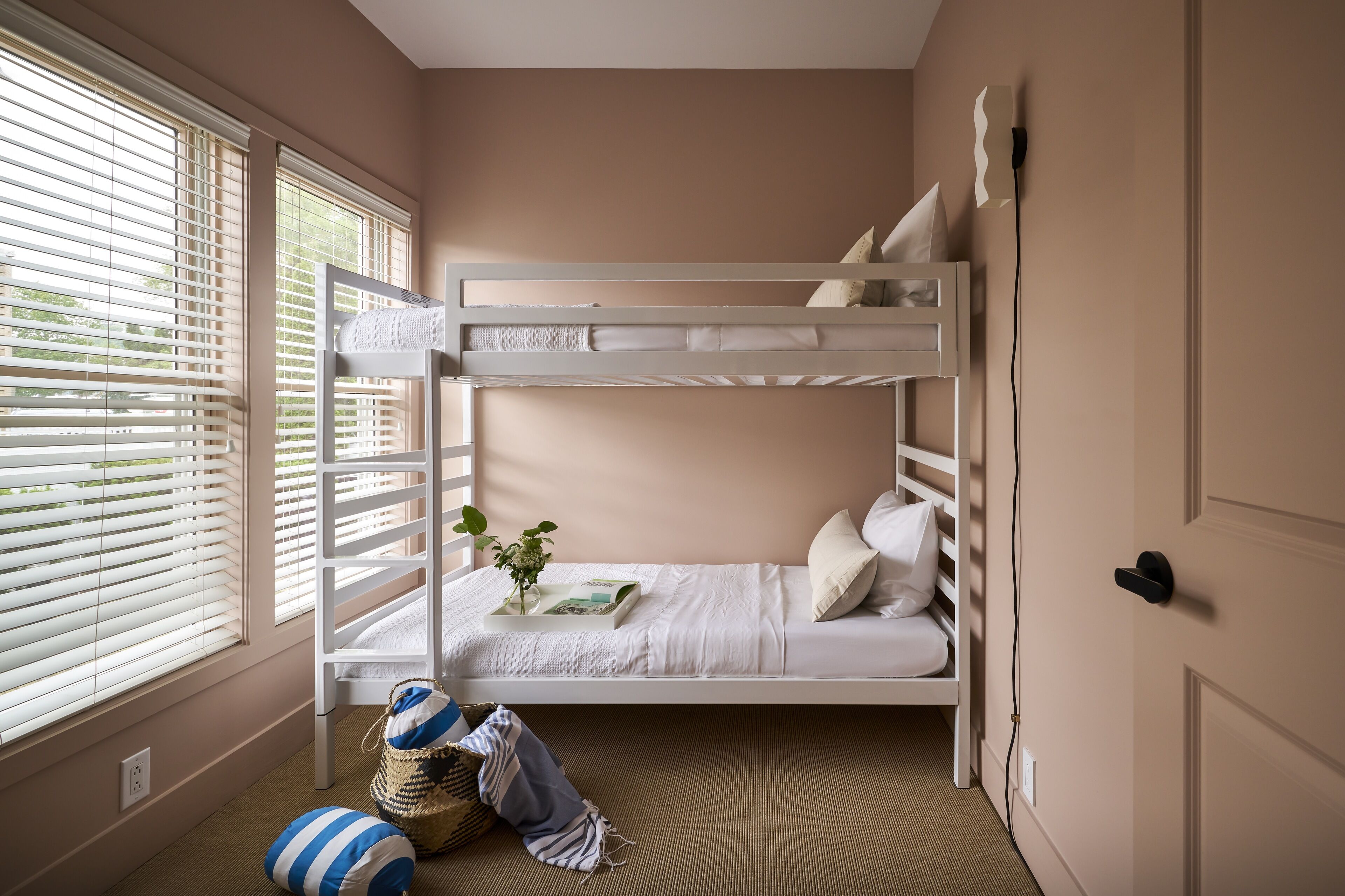 A bunk bed room with a window, a door, and a bedside table with a plant.