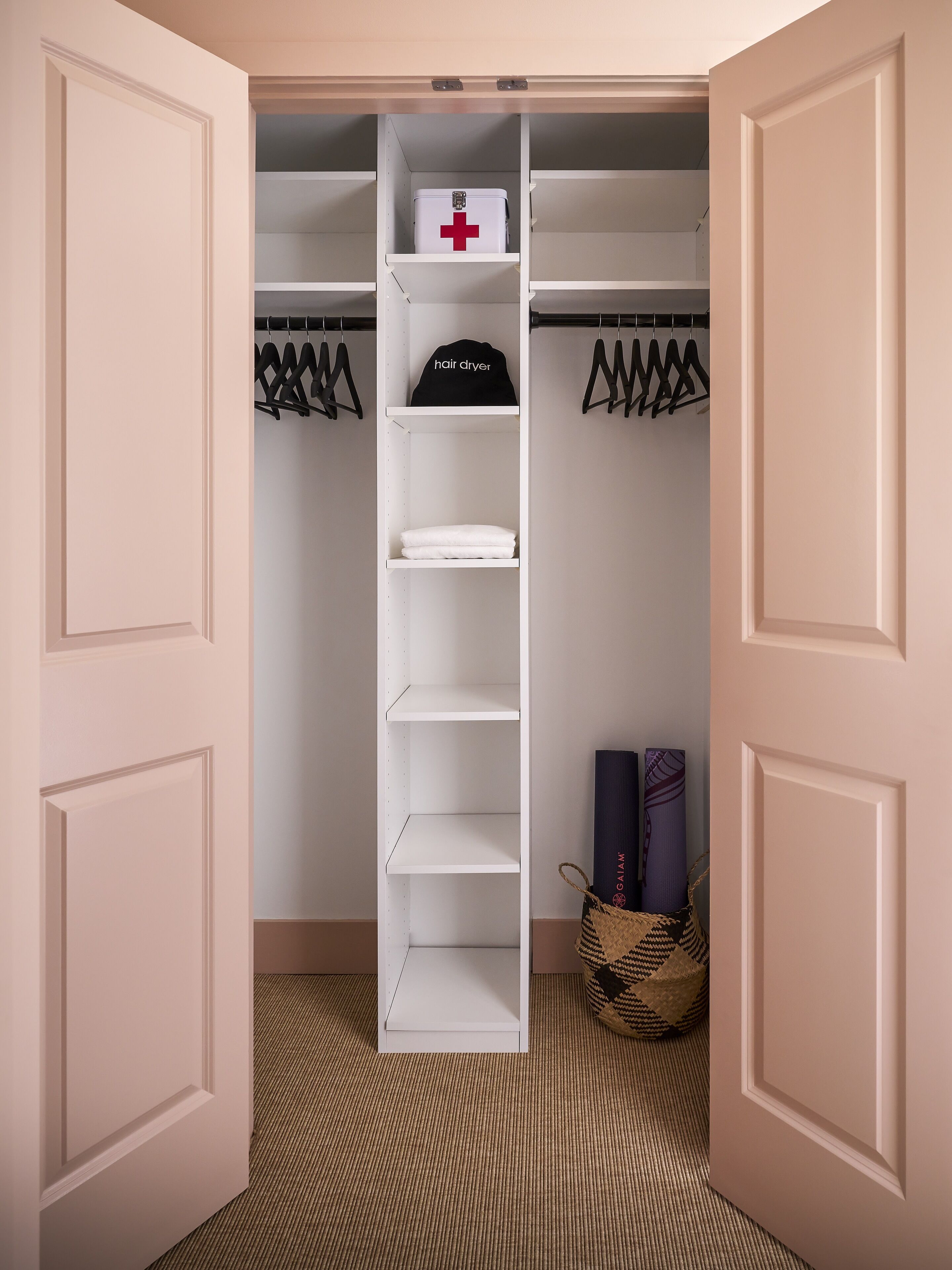 A closet with a white interior, a first aid kit, a hair dryer, and hanging clothes.