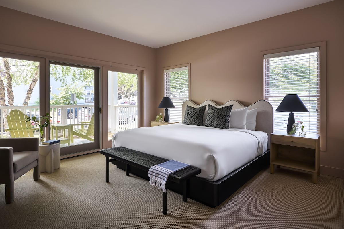 A spacious bedroom with a large bed, a bench, a chair, and a nightstand with lamps.