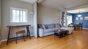 Amplia sala de estar con piso de madera, un sofá gris, una mesa de centro y un comedor con mesa y sillas.